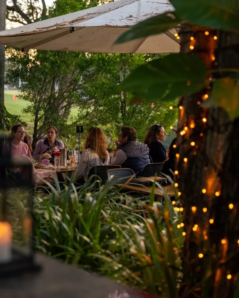 People sitting around cafe tables with fairy light decorations and umbrellas overhead.