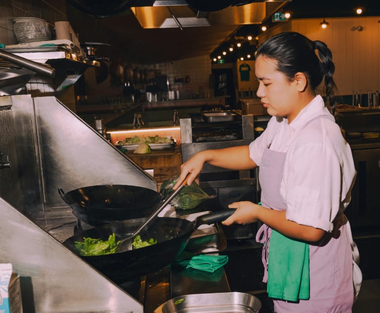 Restaurant staff cooking with a wok over the stove.